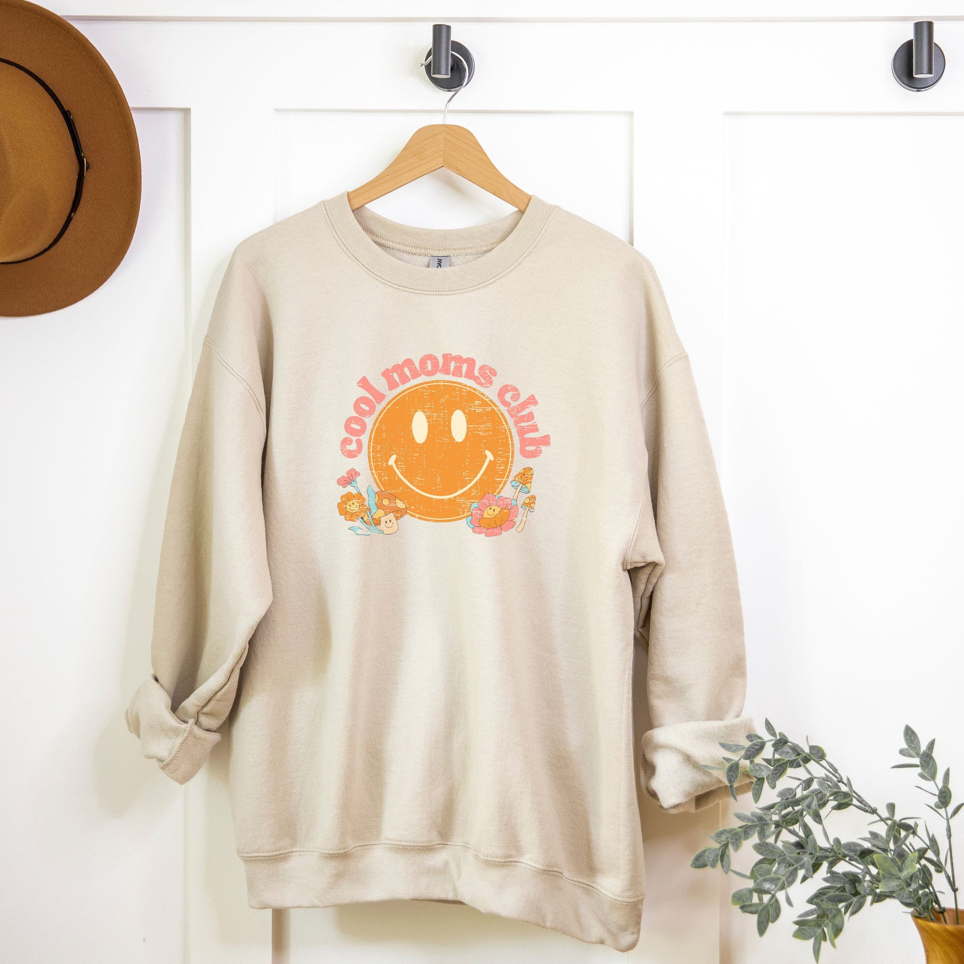 Sand color crewneck sweatshirt with a retro smiley face and mushrooms with vintage pink font that reads: “cool moms club”. Fun Mother’s Day Gift!