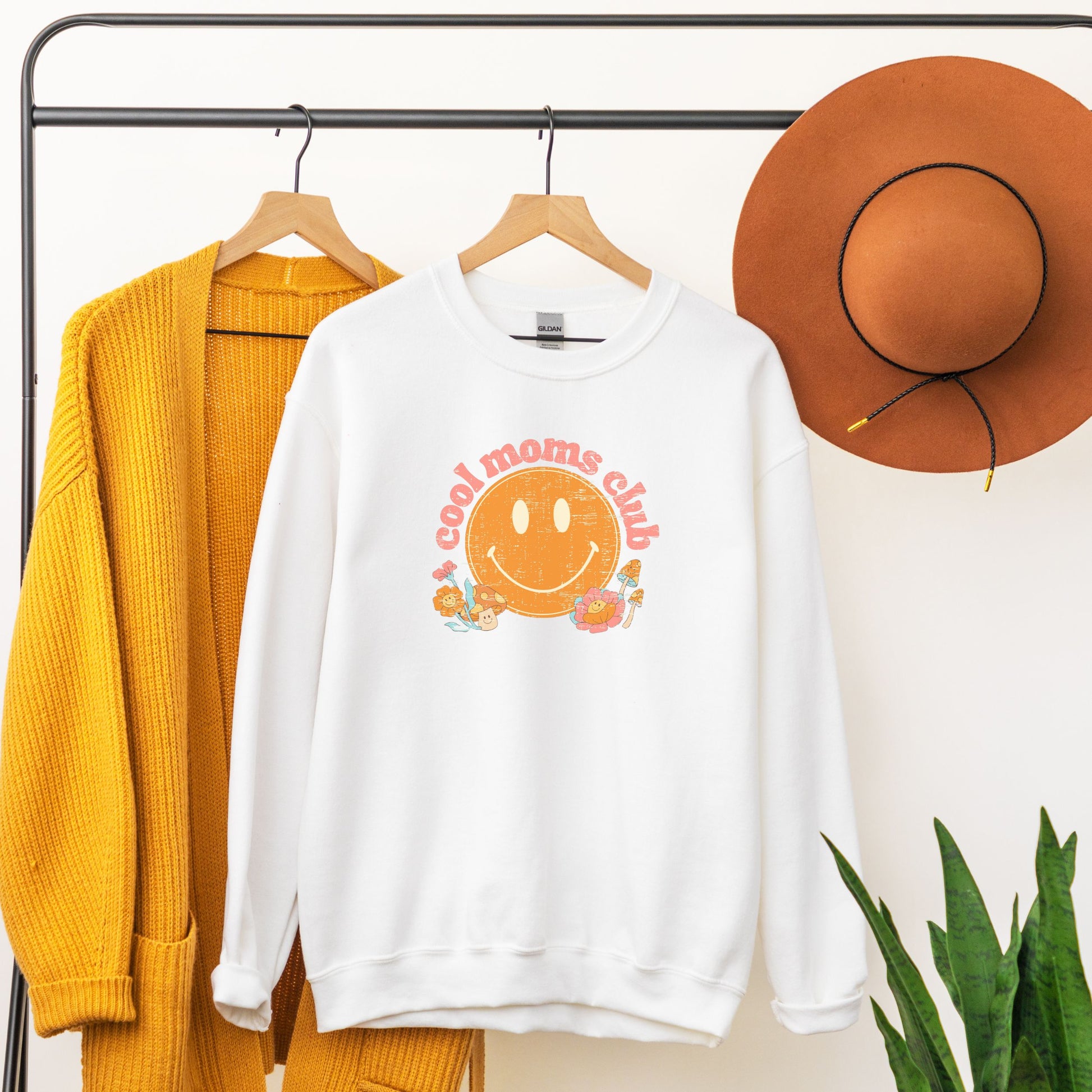 White crewneck sweatshirt with a retro smiley face and mushrooms with vintage pink font that reads: “cool moms club”. Fun Mother’s Day Gift!