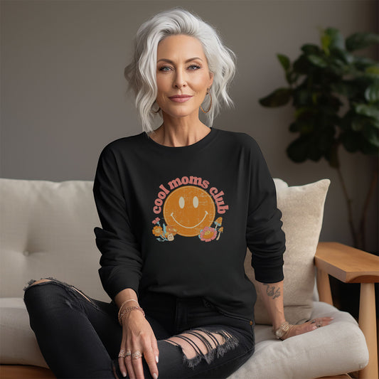 Woman with white hair wearing a black crewneck sweatshirt with a retro smiley face and mushrooms with vintage pink font that reads: “cool moms club”. Fun Mother’s Day Gift!