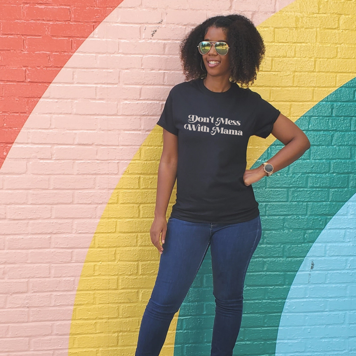 Black woman standing in front of a rainbow wall wearing a black “Don’t Mess With Mama” T-shirt. Mother’s Day Gift!