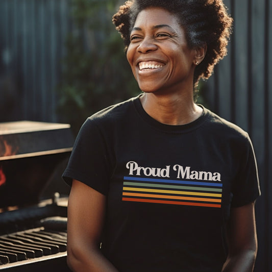 Black woman smiling and wearing a black “Proud Mama” rainbow t-shirt. 