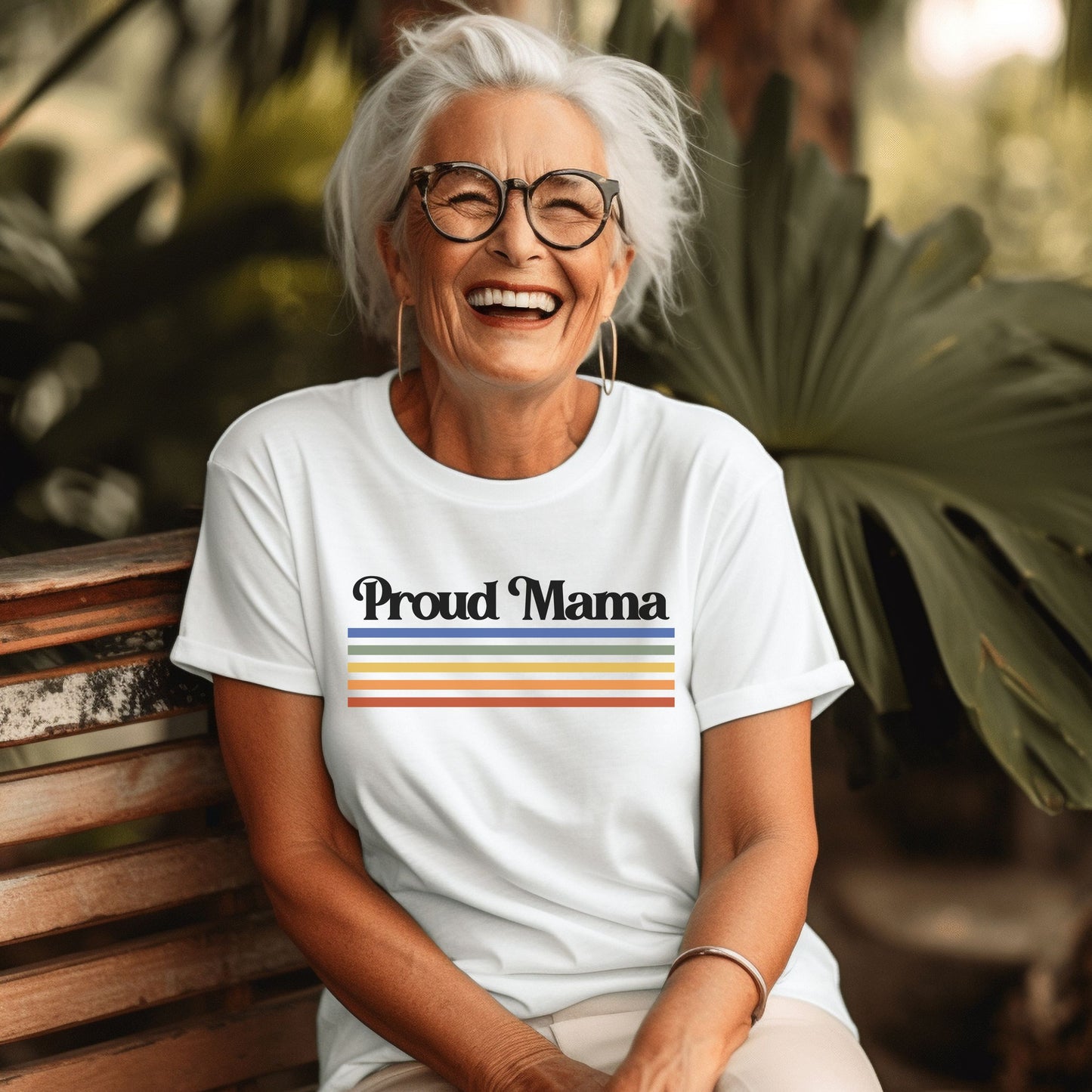 woman with gray hair smiling and wearing a white “Proud Mama” rainbow t-shirt.